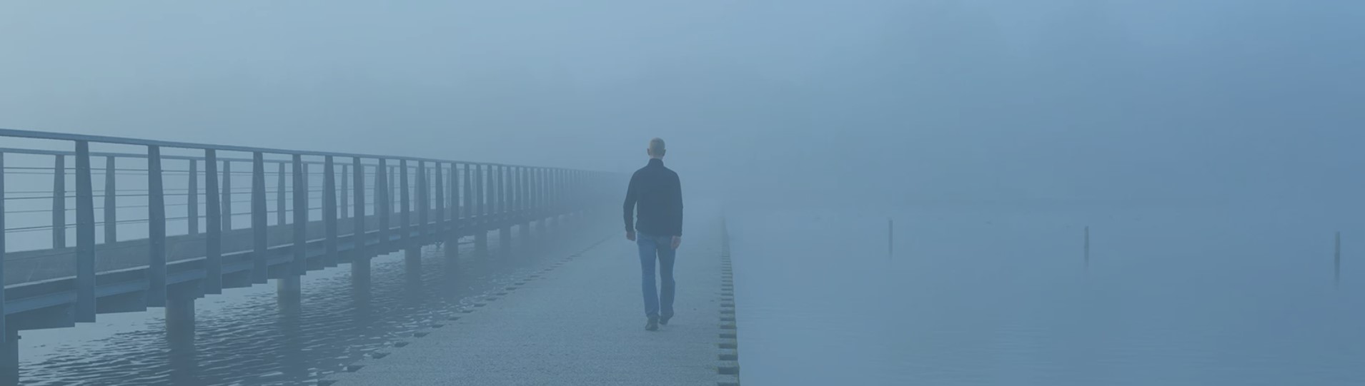 Muž stojící sám na mlhavém molu u vody